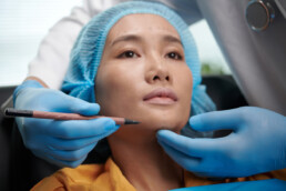 The image shows a doctor marking areas on face of patient before facelift surgery to represent facial implants.