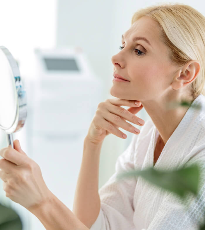 An elder woman patient looking into a hand mirror