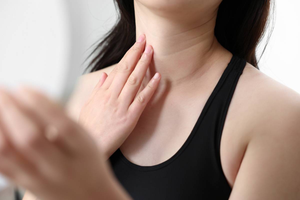 A woman looking in the mirror while touching her neck and wondering, am i too young for a neck lift.