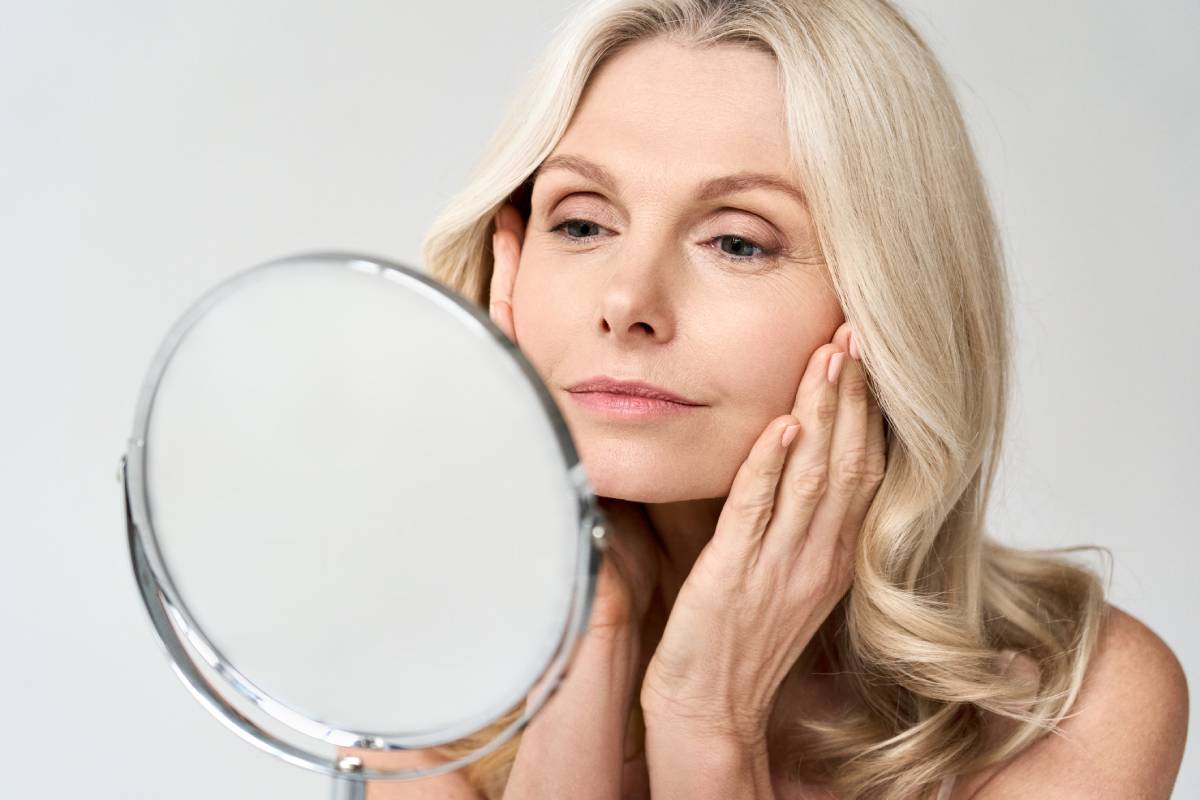 Closeup portrait of woman looking at mirror touching her skin.